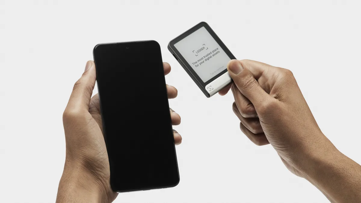 Portefeuille matériel Ledger Flex tenu à côté d'un téléphone